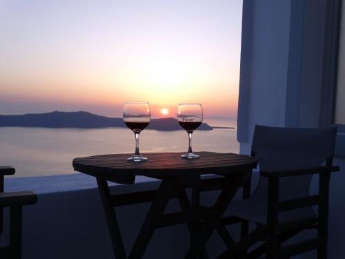 Yposkafo Suites - Studio - Santorini في فيرا: كأسين من النبيذ يجلسون على طاولة مع غروب الشمس