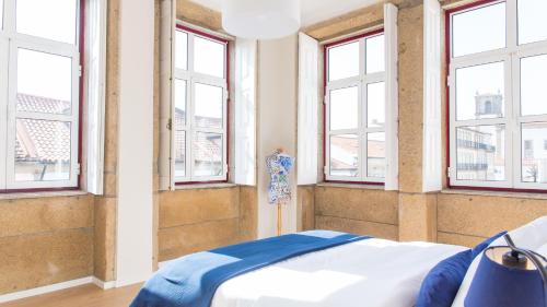 um quarto com janelas e uma cama com lençóis azuis em Praça 44 Boutique Apartments em Braga