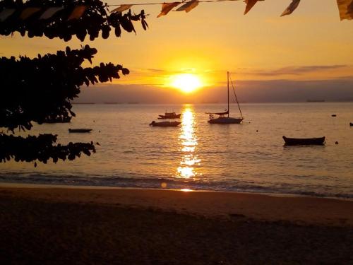 a sunset on the beach with boats in the water at Nena's Suítes in Praia de Araçatiba
