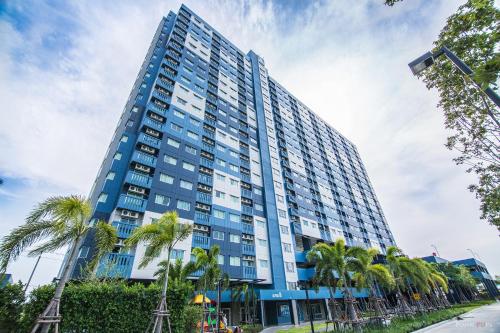 a tall blue building with palm trees in front of it at Lumpini LOFT condo 1705 in Ban Sahakham