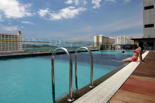 una mujer sentada en el borde de una piscina en Horizon Hotel, en Kota Kinabalu