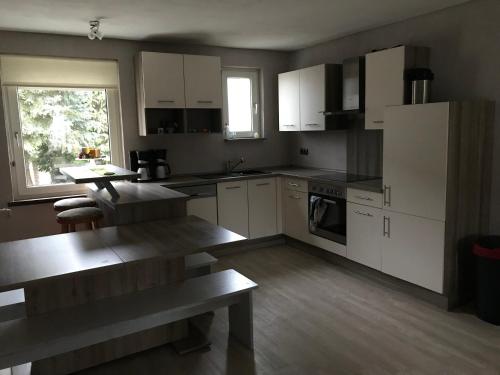 une cuisine avec des placards blancs, une table et une fenêtre dans l'établissement Haus Irmgard, à Schlierschied