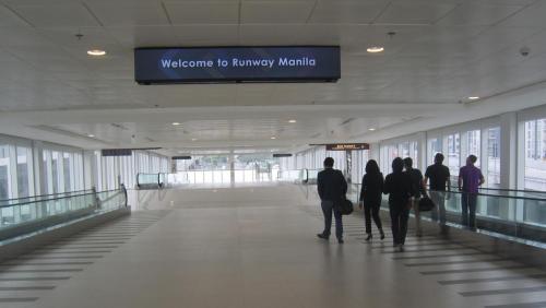 a group of people walking down a hallway in an airport at One Palm Tree Villas in Manila