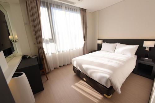 a bedroom with a large white bed and a window at Geoje Artnouveau Suite Hotel in Geoje 