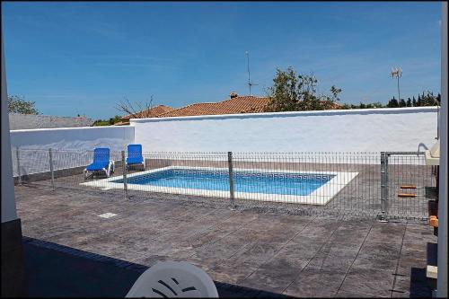 a swimming pool with two blue chairs next to a fence at Casa Rural Zara III in Conil de la Frontera