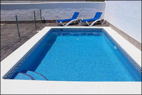 a swimming pool with two blue chairs next to a building at Casa Rural Zara III in Conil de la Frontera