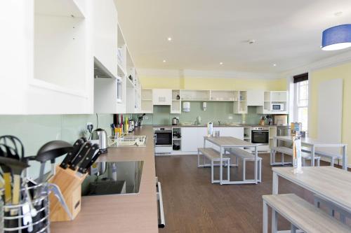 una cocina con armarios blancos, mesas y sillas en YHA Swanage en Swanage