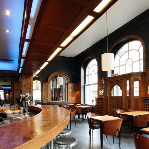 a restaurant with a bar and tables and windows at Hotel La Royale in Leuven