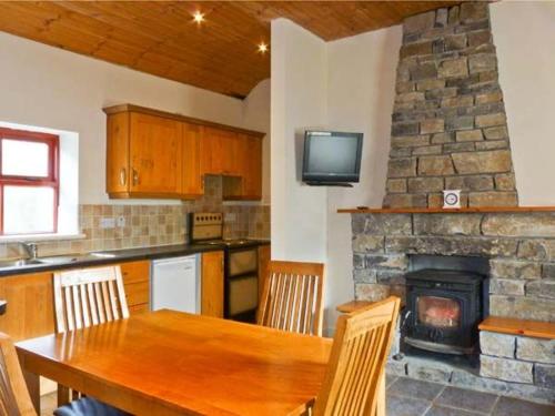 cocina con mesa de madera y chimenea de piedra en Cavan Hill Cottage, en Ballinrobe
