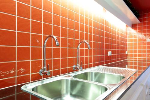a kitchen sink with two faucets on a red tiled wall at Smile Inn in Bangkok