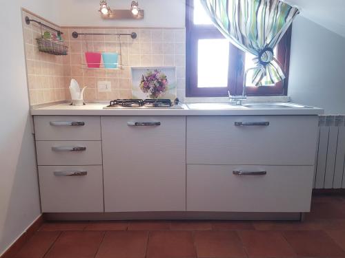 cocina blanca con fregadero y ventana en Mansarda con Vista Piscina, en Campofelice di Roccella