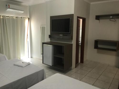 a living room with a tv and a bed and a room at Hotel Comodoro in Vilhena