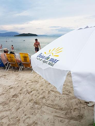 a white umbrella on the beach with people in the water at Apart Hotel Beira do Mar in Florianópolis