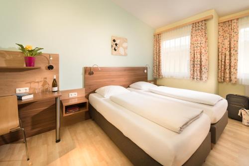 two beds in a hotel room with a desk and window at Hotel Radlinger in Pellendorf
