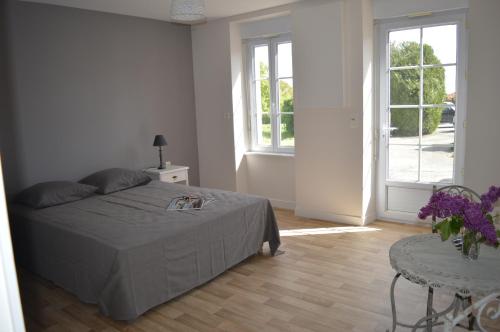 Schlafzimmer mit einem Bett, einem Tisch und Fenstern in der Unterkunft Gite de la Foye - La Couleur des prés in Combrand