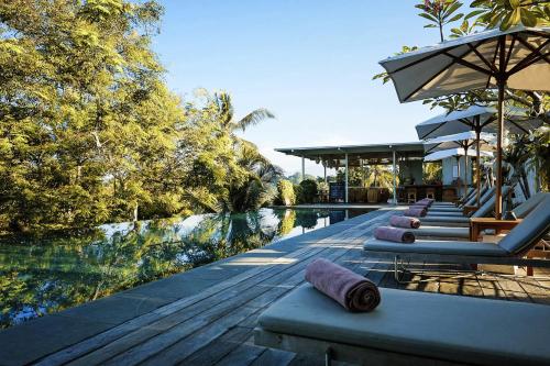 a row of lounge chairs on a deck next to a pool at Bisma Eight - CHSE Certified in Ubud
