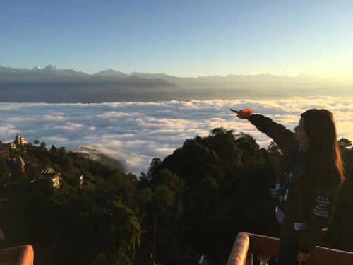 a woman standing on top of a mountain with her arm up at Peaceful Cottage & Cafe Du Mont in Nagarkot