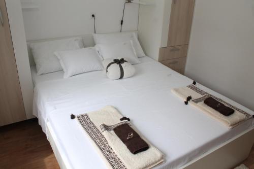 a white bed with a purse and two bags on it at Apartman Bombon in Selce