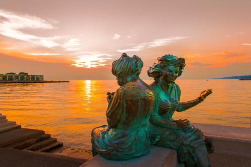 a statue of two women sitting next to the water at sunset at Residence Theresia- Tailor Made Stay in Trieste