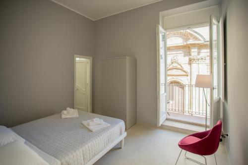 a bedroom with a bed and a red chair and a window at Ortigia Casa Fab in Siracusa