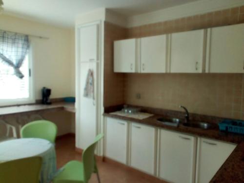 uma cozinha com armários brancos e cadeiras verdes e uma mesa em villa avec jardin em Saïdia