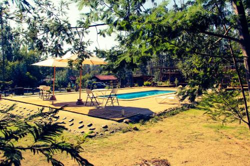 einen Pool mit Sonnenschirm, Tisch und Stühlen in der Unterkunft El Bosque Lodge in Algarrobo