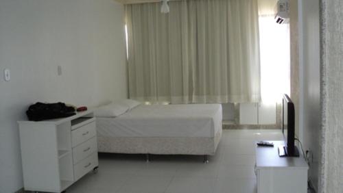 a bedroom with a bed and a dresser and a window at Studio na praia da Barra in Salvador