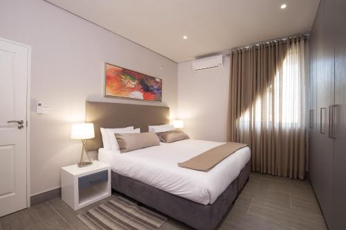 a bedroom with a large white bed and a window at City Mews On Independence in Gaborone