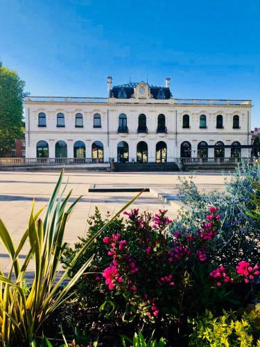 un grand bâtiment blanc avec des fleurs roses devant lui dans l'établissement ★ Studio ★ Brive Centre ★, à Brive-la-Gaillarde
