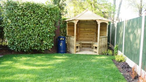 a wooden gazebo in a yard next to a fence at The Lawn Guest House Gatwick in Horley