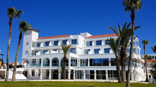 a white building with palm trees in front of it at Akti Beach Hotel & Village Resort in Paphos City