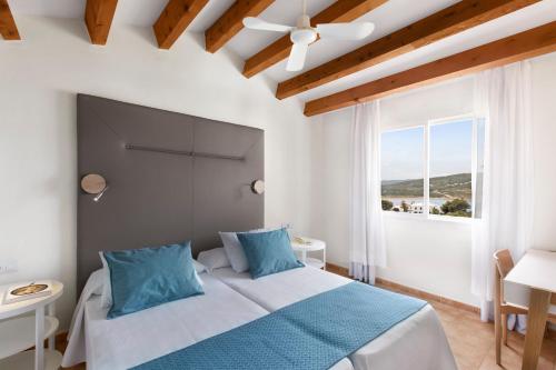 a bedroom with a bed with blue pillows and a window at TRH Tirant Playa in Fornells