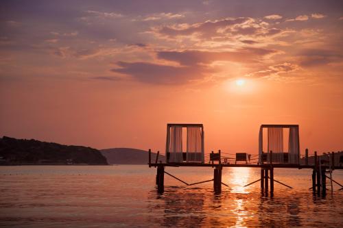 a dock with two chairs on the water at sunset at Sirene Luxury Hotel Bodrum in Yalıkavak