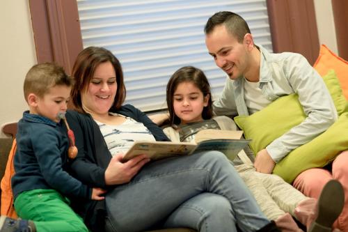 a family sitting on a couch reading a book at HI Tournai Hostel in Tournai