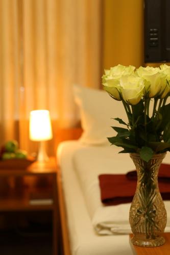a vase filled with white roses on a table next to a bed at Hotel AI Königshof in Berlin