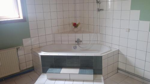 a white tiled bathroom with a bath tub with a vase at Stadtschenke in Villach