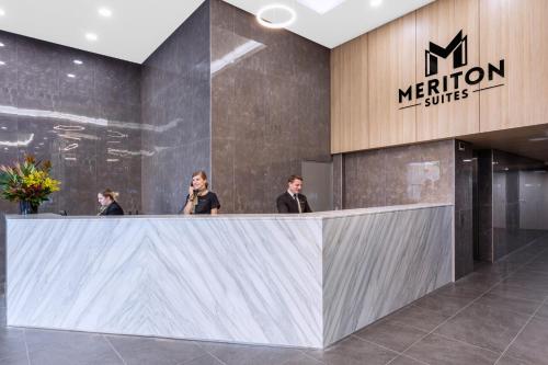 3 persone in piedi al bancone della reception in una hall di Meriton Suites Waterloo a Sydney