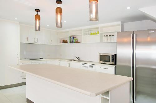 a kitchen with white cabinets and a stainless steel refrigerator at Gosamara Apartments in Byron Bay