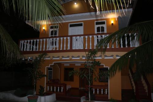 a yellow house with a white balcony and palm trees at El Shaddai in Mannar