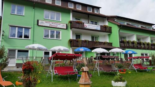 a green building with chairs and umbrellas in front of it at Hotel-Pension Dressel in Warmensteinach