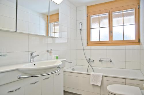 a white bathroom with a sink and a tub and a toilet at Apartment Alpha - GRIWA RENT AG in Grindelwald