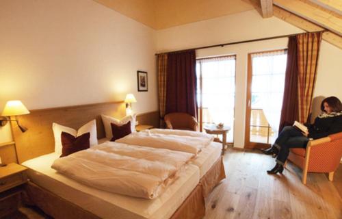 a bedroom with a large bed and a woman sitting in a chair at Naturparkhotel Schwarzwaldhaus in Bernau im Schwarzwald