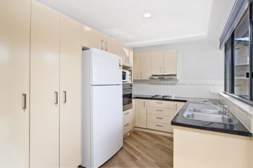 a kitchen with white cabinets and a white refrigerator at Flightdeck 301 5-7 Clarence Street in Port Macquarie