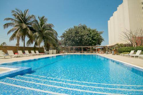 a swimming pool with chairs and palm trees and a building at Novotel Dakar in Dakar