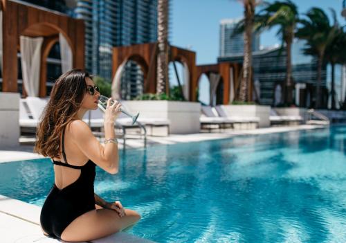 a woman in a black dress sitting next to a swimming pool at SLS LUX Brickell in Miami