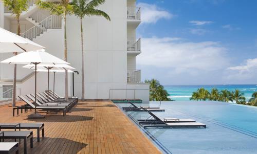 an image of a resort swimming pool with chairs and the ocean at 'Alohilani Resort Waikiki Beach in Honolulu