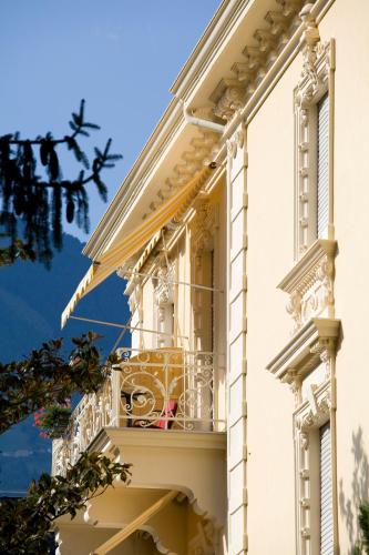 a white building with a balcony with a table at Hotel Villa Westend in Merano