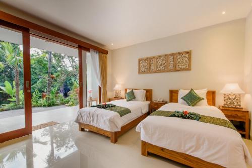 a bedroom with two beds and a large window at Taman Amartha Hotel in Ubud