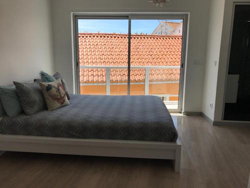a bed in a room with a large window at Loft-Entre a praia e o campo in Nazaré