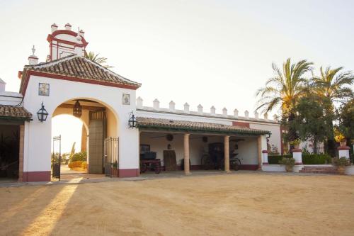 a large white building with an arch and palm trees at Hacienda de Orán in Utrera